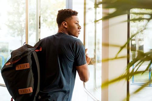 young african american male student with a back pack walking through a door