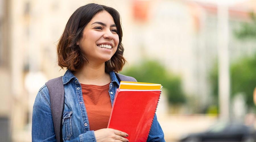 young Latino female student with a backpack holding notebooks and smiling