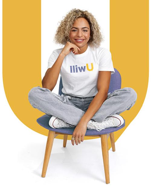 一个有着中等肤色和金色卷发的女人穿着一件白色t恤，上面写着Uwill. 她坐在椅子上微笑着.